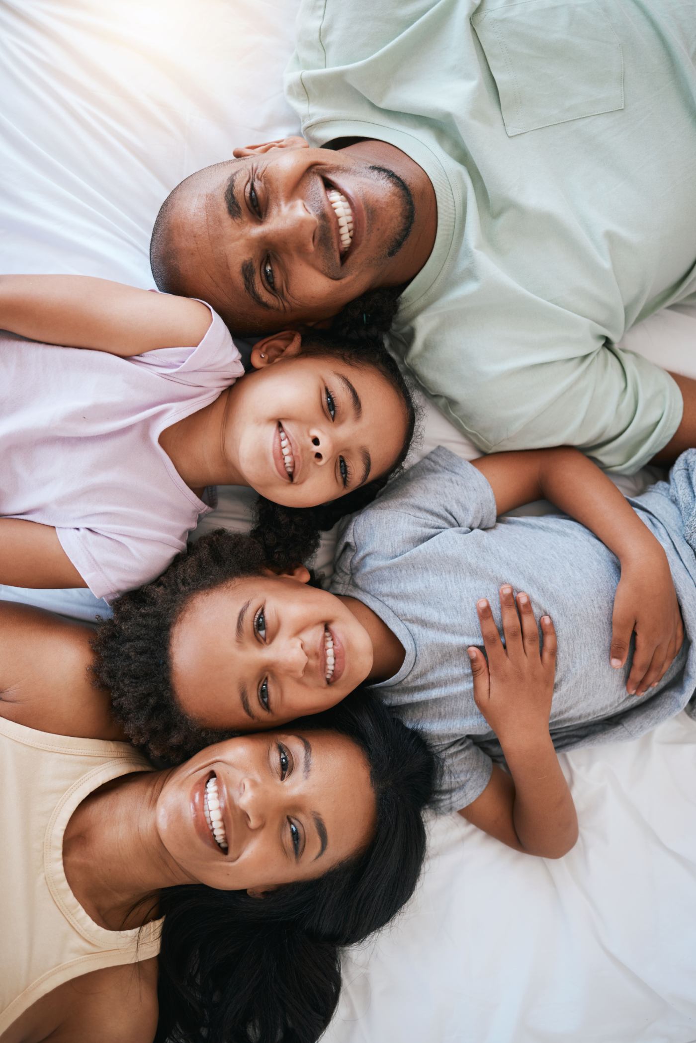 Family of four smiling together on a bed, showcasing a joyful moment of connection, relevant to pediatric dental care and positive experiences for children.