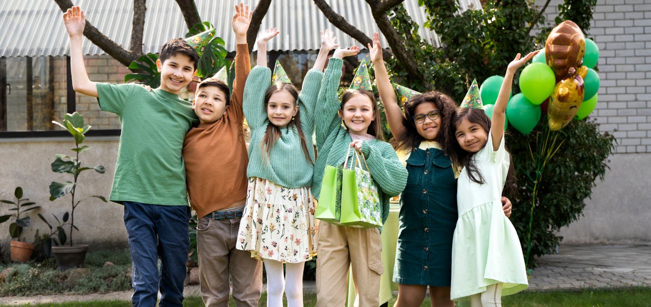 Group of children celebrating with party hats, smiling and holding gift bags, in a festive outdoor setting, emphasizing joy and community engagement in pediatric dental health.
