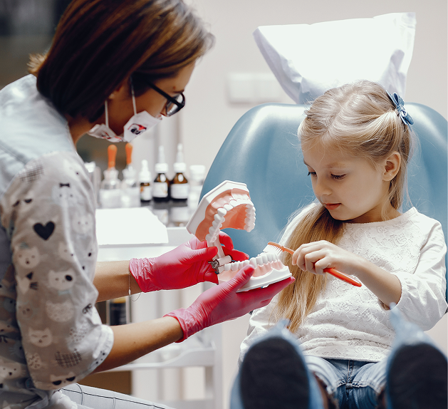 Pediatric dentist demonstrating proper brushing techniques to a young girl using a dental model in a child-friendly dental office.